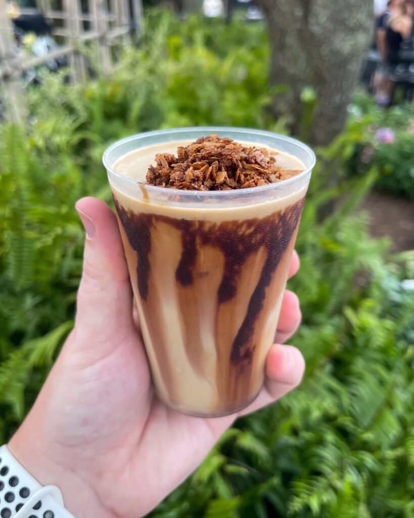 A visually stunning image of Kristoff Kaffe, a frozen coffee masterpiece topped with coffee-chocolate crunch and served in a clear glass, ready to be enjoyed.